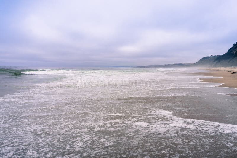 Νερό που καλύπτει μια αμμώδη παραλία στην ακτή Ειρηνικών Ωκεανών σε ένα ομιχλώδες απόγευμα, Καλιφόρνια